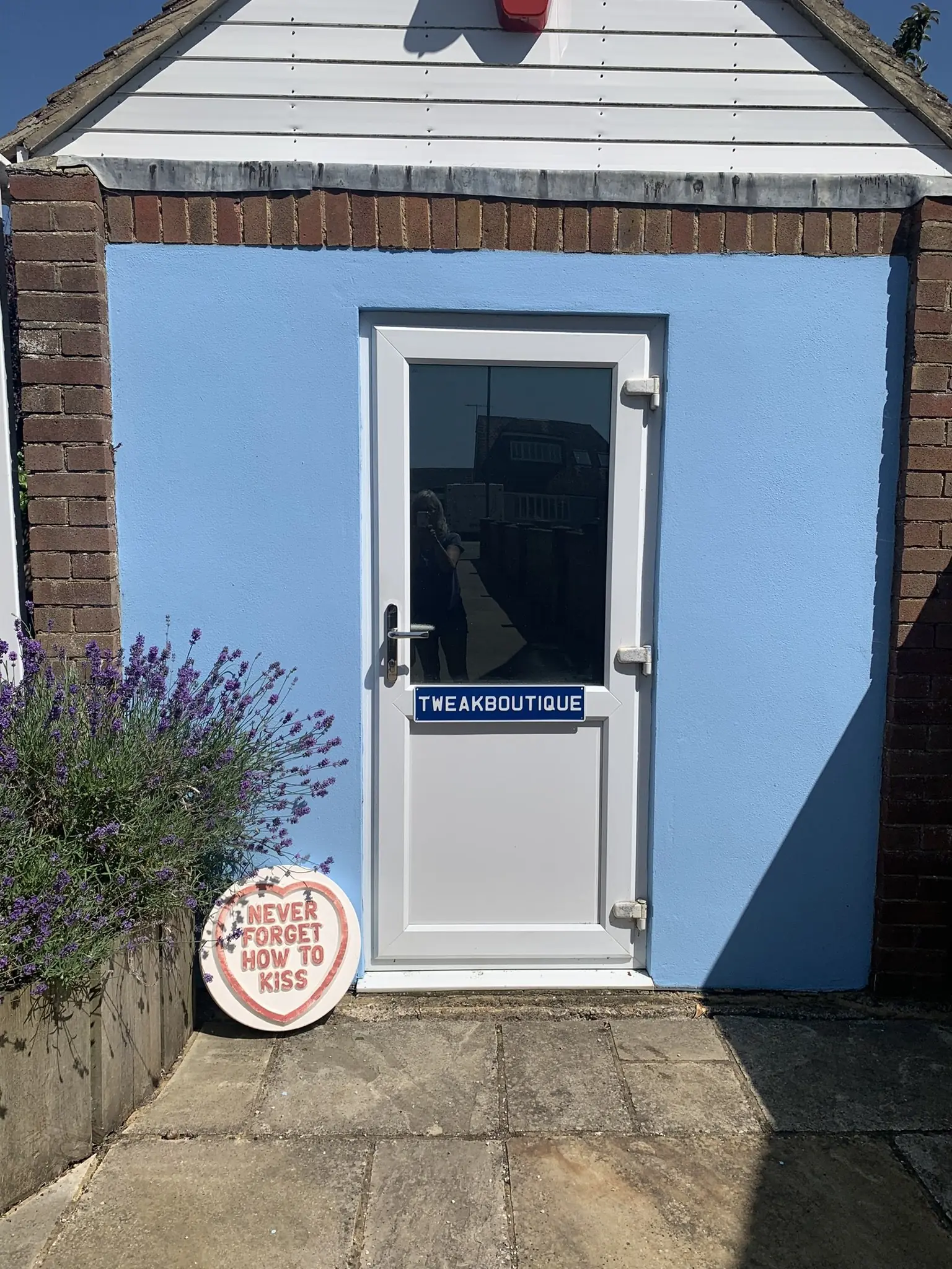 The blue door of the TweakBoutique clinic, with its name plate and lavender beside the step