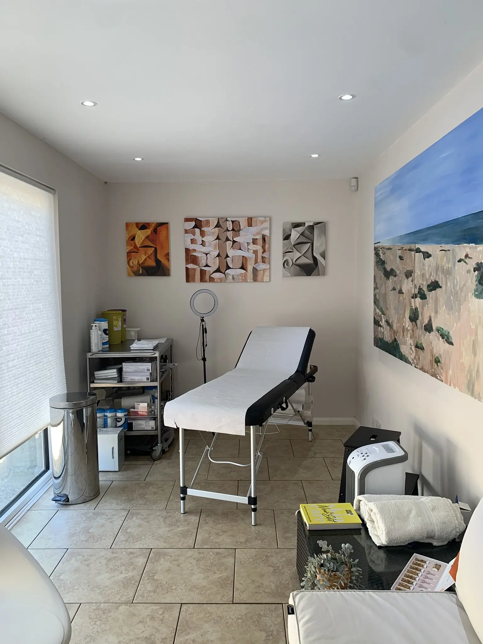 The TweakBoutique treatment room: a couch made up with fresh paper, a trolley of supplies and a painting of the coast
