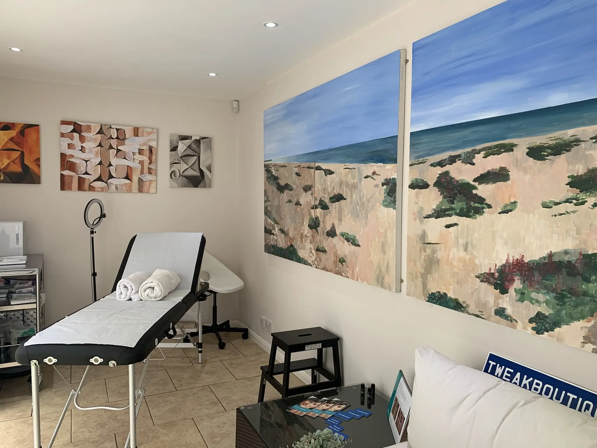 The TweakBoutique treatment room: a couch with rolled towels beneath two large paintings of the beach