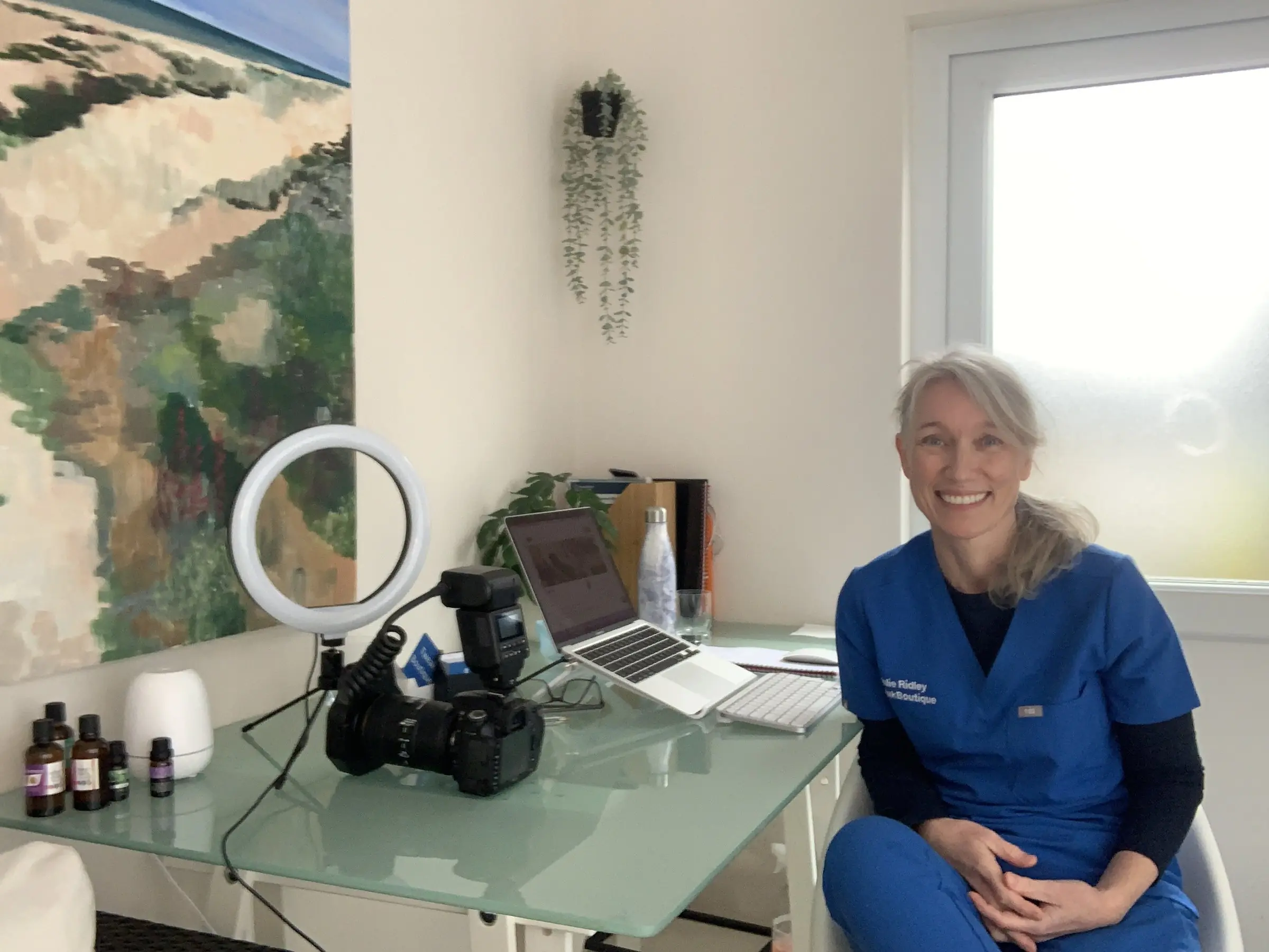 Dr Julie Ridley smiling at her desk in the clinic, wearing her blue TweakBoutique scrubs